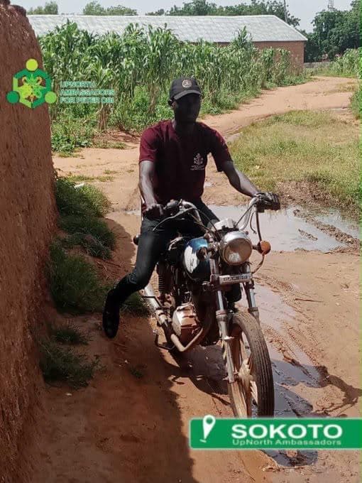 An ambassador riding a motorcycle along a rural track to reach a community.